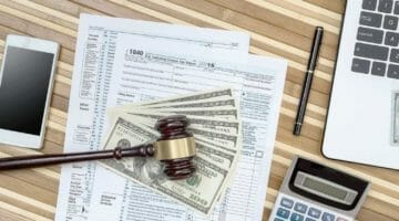 forms, cash, and gadgets on a table | What Tax Forms Do I Need for a New Employee? | Featured