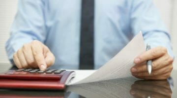 businessman using calculator and reading document | Tax Considerations According To Type Of Business Ownership | types of business ownership | taxing business | Featured